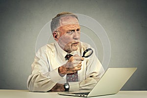 Senior man working looking through magnifying glass at laptop screen