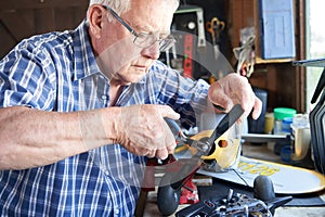 Senior Man Working On Model Radio Controlled Aeroplane In Shed At Home