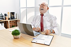 Senior man working at the office using computer laptop angry and mad screaming frustrated and furious, shouting with anger