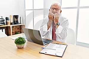 Senior man working at the office using computer laptop laughing and embarrassed giggle covering mouth with hands, gossip and