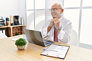 Senior man working at the office using computer laptop laughing nervous and excited with hands on chin looking to the side