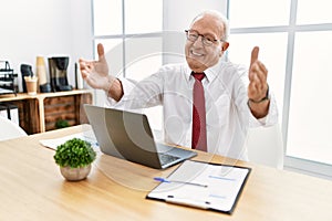 Senior man working at the office using computer laptop looking at the camera smiling with open arms for hug