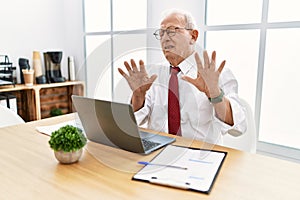 Senior man working at the office using computer laptop moving away hands palms showing refusal and denial with afraid and
