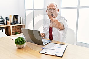 Senior man working at the office using computer laptop pointing displeased and frustrated to the camera, angry and furious with