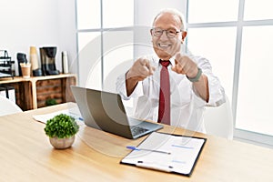 Senior man working at the office using computer laptop pointing to you and the camera with fingers, smiling positive and cheerful
