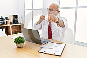 Senior man working at the office using computer laptop punching fist to fight, aggressive and angry attack, threat and violence