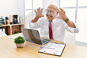 Senior man working at the office using computer laptop shouting frustrated with rage, hands trying to strangle, yelling mad