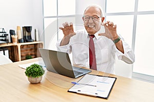 Senior man working at the office using computer laptop smiling funny doing claw gesture as cat, aggressive and sexy expression