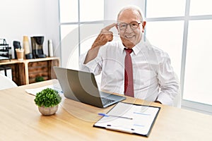 Senior man working at the office using computer laptop smiling pointing to head with one finger, great idea or thought, good