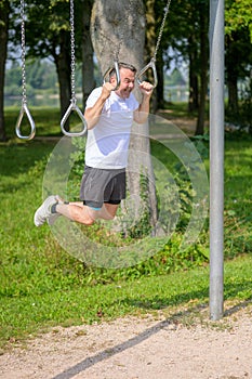 Senior man working out on exercise rings in a park