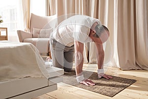 Senior man working out at home in living room, doing yoga exercise on mat.