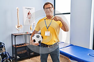 Senior man working at sport physiotherapy clinic pointing finger to one self smiling happy and proud