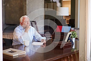 Senior Man Writing Memoirs In Book Sitting At Desk