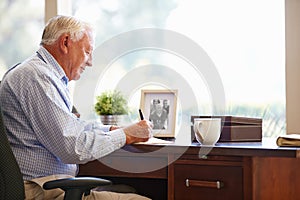 Senior Man Writing Memoirs In Book Sitting At Desk