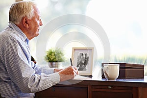 Senior Man Writing Memoirs In Book Sitting At Desk photo