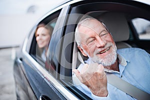 Senior man and young woman sitting in car, looking out of window.