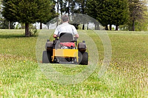 Senior man on zero turn lawn mower on turf