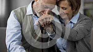 Senior married people sitting together holding hands on walking stick, closeness photo