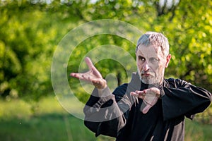 Senior master practicing qiqong taijiquan in the wild forest. Breathing exercise and martial art moves, traditional chinese qi en