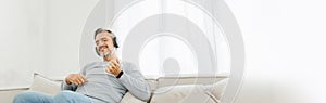 Senior mature adult man listening to music with headphones playing air guitar