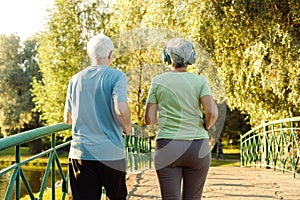 Senior mature couple running together in the park looking at each other while jogging slimming exercises.