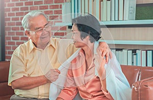 Senior mature couple is taking care by husband putting on Blanket for his wife on Sofa at home. for elder togetherness