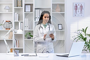 Senior mature female doctor serious and confident thoughtfully using tablet computer, Latin American woman in medical