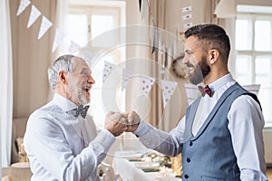 A senior and mature man standing indoors in a room set for a party, making fist bump.