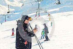 Senior mature skier making selfie with modern camera phone at winter alpine skiing resort. Old aged sporty person using smartphone
