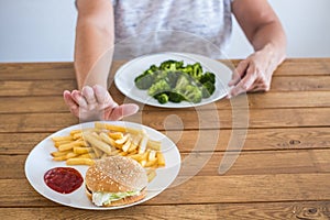 Senior and mature woman choosing broccoli and not hamburger - healthy and diet lifestyle concept to lose weight or be more healthy