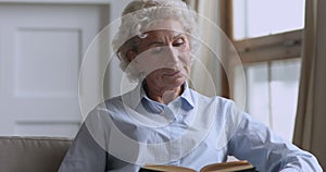 Senior mature woman reading book relaxing on sofa at home