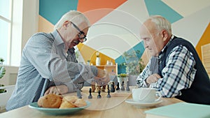 Senior men friends busy with chess game talking and playing in modern house