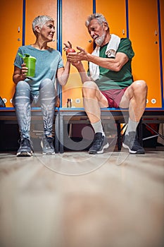 Senior man and woman sitting in gym locker room, talking and sharing an apple photo