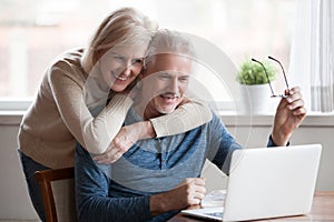 Senior middle aged happy couple embracing using laptop together