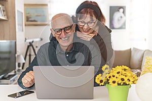 Senior middle aged happy couple embracing using laptop together -  smiling elderly family reading the news and shopping online