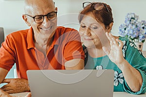 Senior middle aged happy couple embracing using laptop together - smiling elderly family reading the news and shopping online from