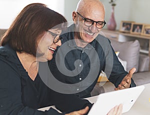 Senior middle aged happy couple embracing using tablet together -  smiling elderly family reading the news and shopping online