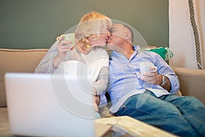 Senior mixed race couple kissing on couch in front of a laptop