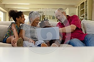 Senior mixed race couple sitting on the couch with their young grandson and granddaughter