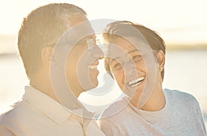 A senior mixed race couple walking together on the beach smiling and laughing on a day out at the beach. Hispanic