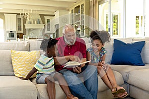 Senior mixed race man sitting on the couch with his young grandson and granddaughter