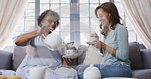 Senior mixed race woman drinking tea with her daughter in social distancing