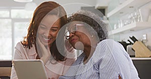 Senior mixed race woman using a digital tablet with her daughter, in social distancing