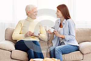 Senior mom and adult daughter talking and drinking coffee