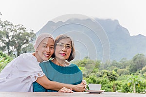 Senior mother and adult daughter are hugging traveling together with mountain view in background.