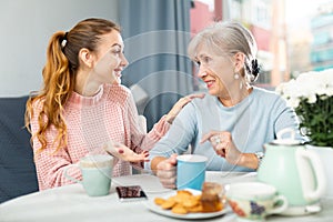 Senior mother and adult granddaughter having conversation and drinking tea