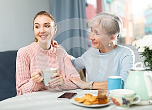 Senior mother and adult granddaughter having conversation and drinking tea