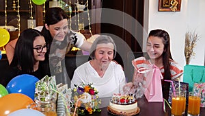 Senior mother with daughter and granddaughters blowing candles on birthday cake