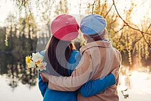 Senior mother with flowers and her adult daughter hugging by spring river. Mother`s day concept. Family values