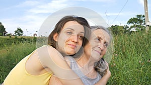 Senior mother with gray hair with her adult daughter in the garden hugging each other during picnic during sunny day
